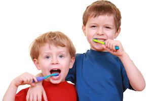 Two boys brush their teeth infront of a white backdrop | Workman Family Dental